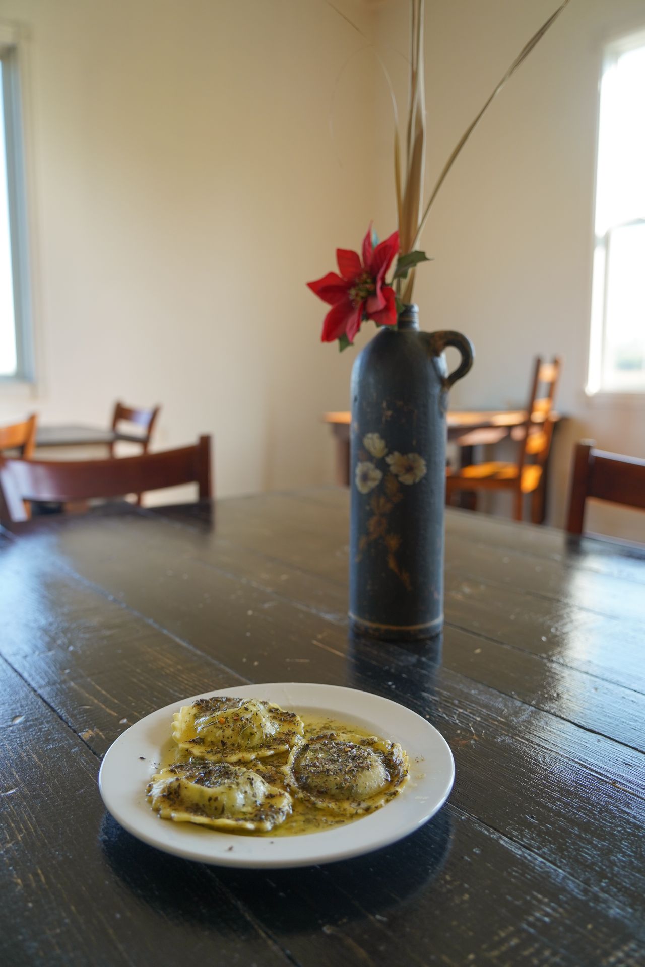 A plate of 3 raviolis and a vase with flowers at Chef Stan's Place