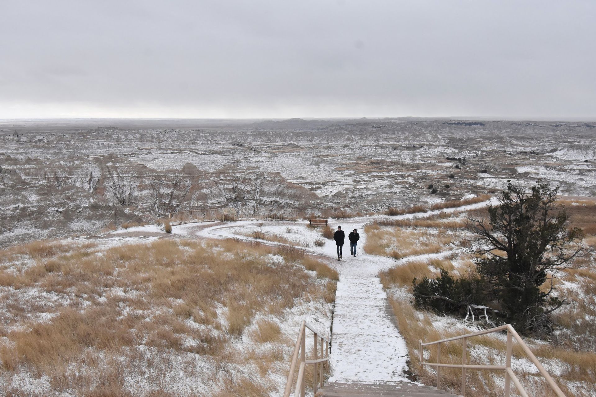 Two people walking on a snowy path at Pinnacles Overlook in Badlands National Park