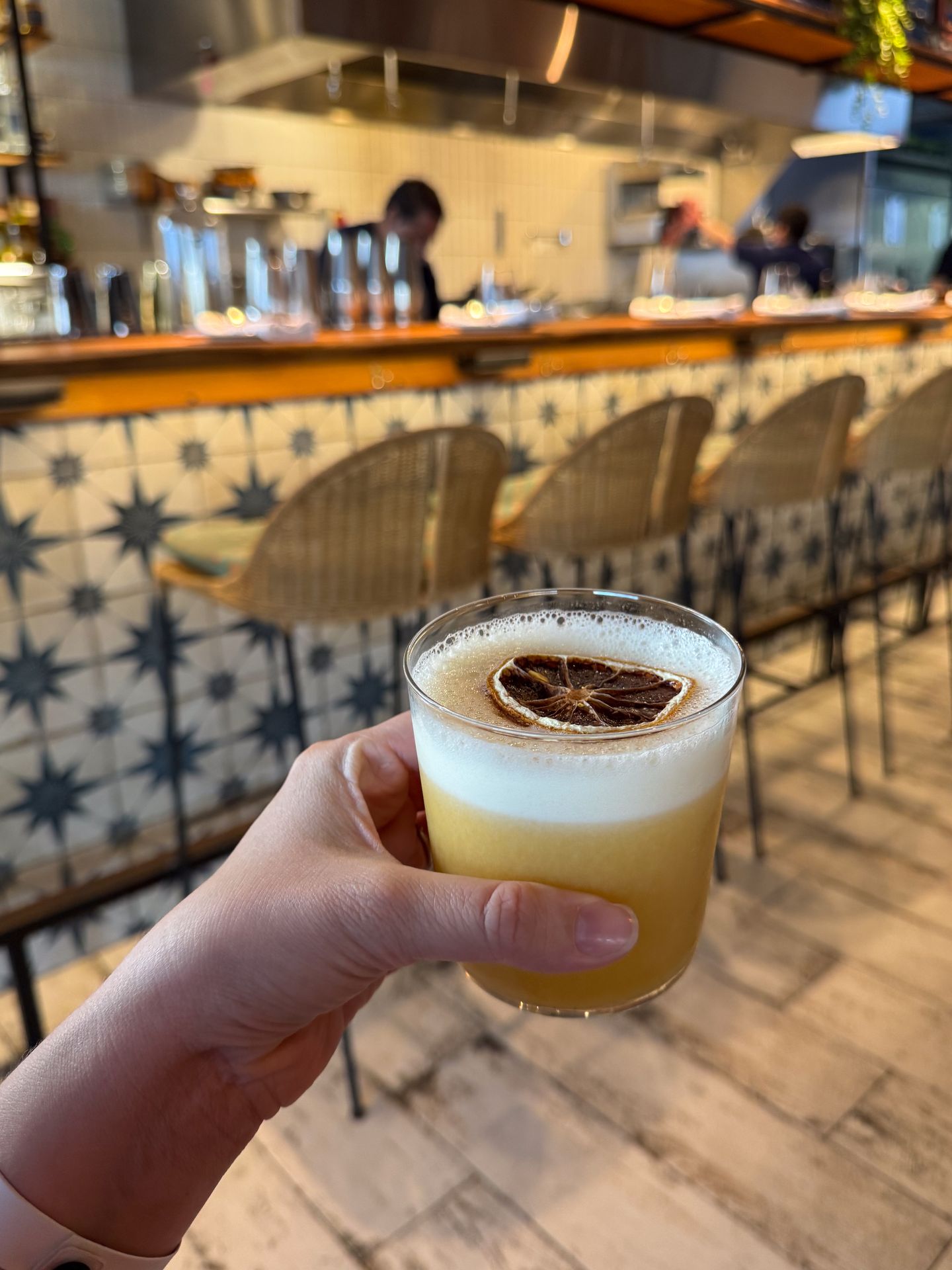 A cocktail in front of a bar with blue and white tiles at Lima Bistro