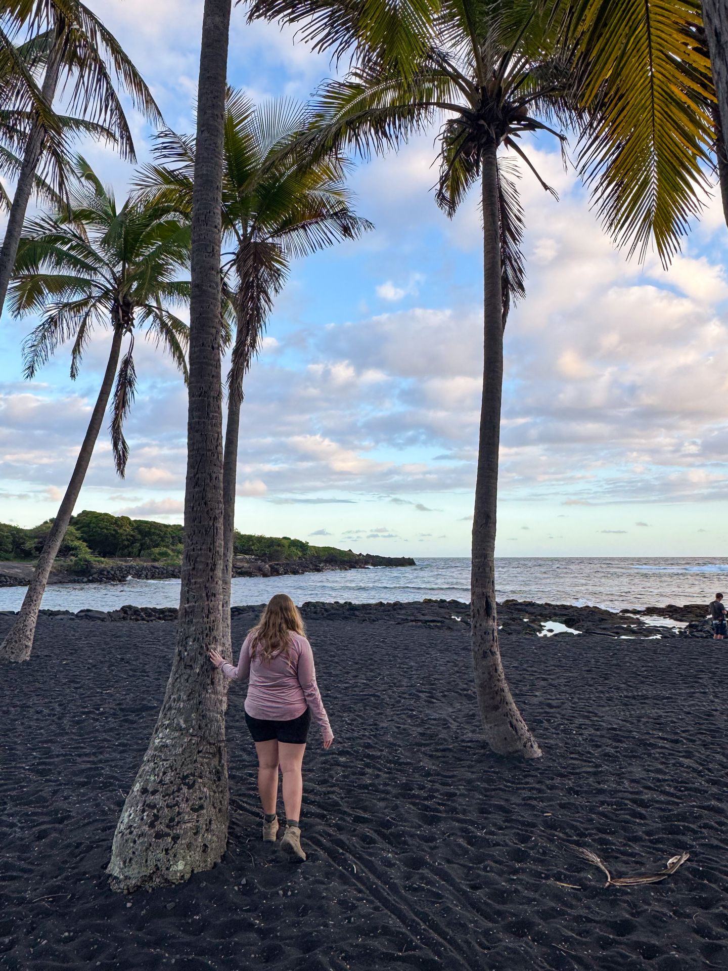 Lydia standing next to a palm tree on a black sand beach