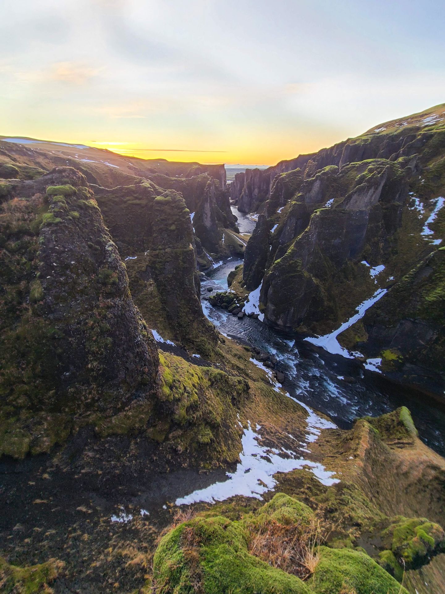 Looking down a rocky, green canyon with a sunrise in the background.