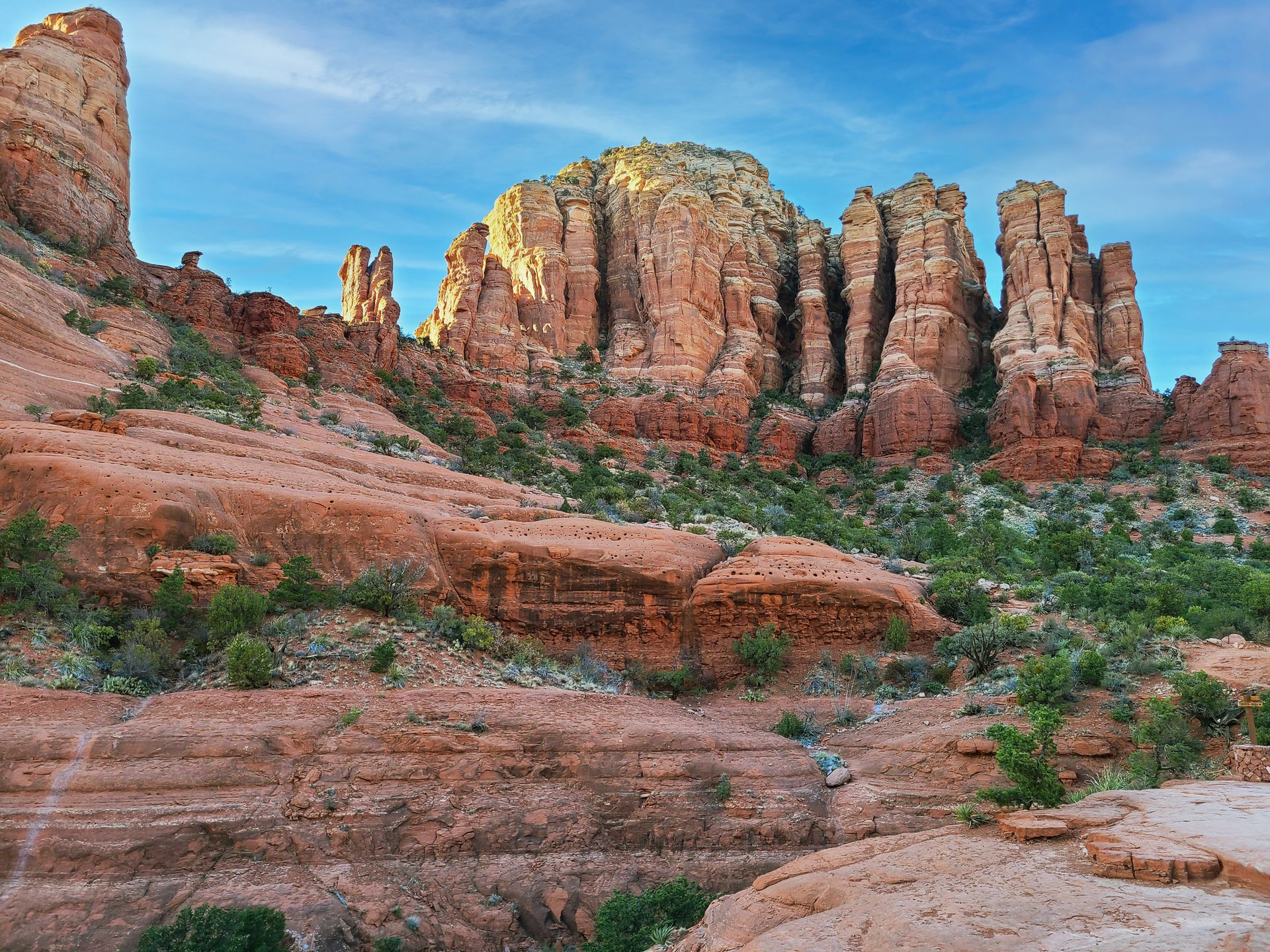 An orange rock face with white stripes and green trees scattered throughout. This is Chicken Point and was taken on a Sedona pink Jeep tour.
