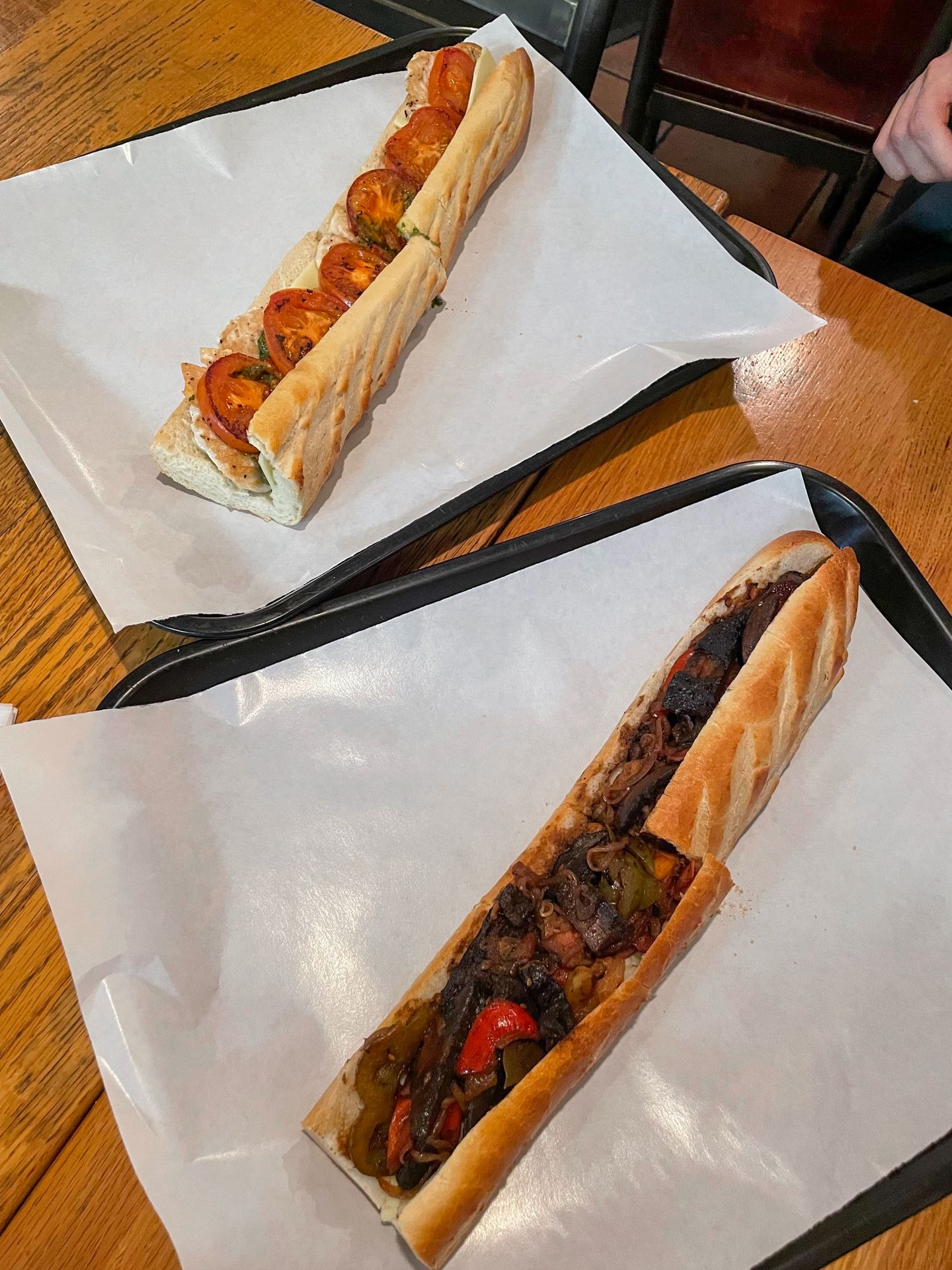 Two large subs from Dino's Cafe. One has veggies and the other has chicken and tomatoes.