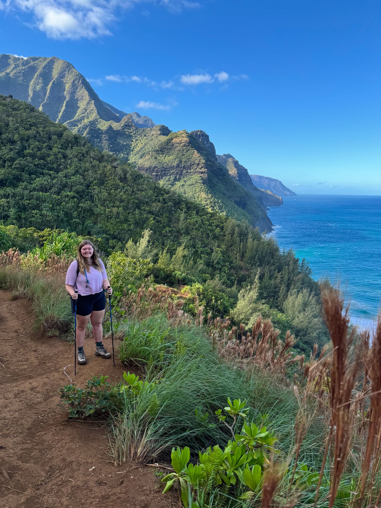 Lydia standing high above the ocean on a cliff while hiking along the coast in Ha'ena State Park