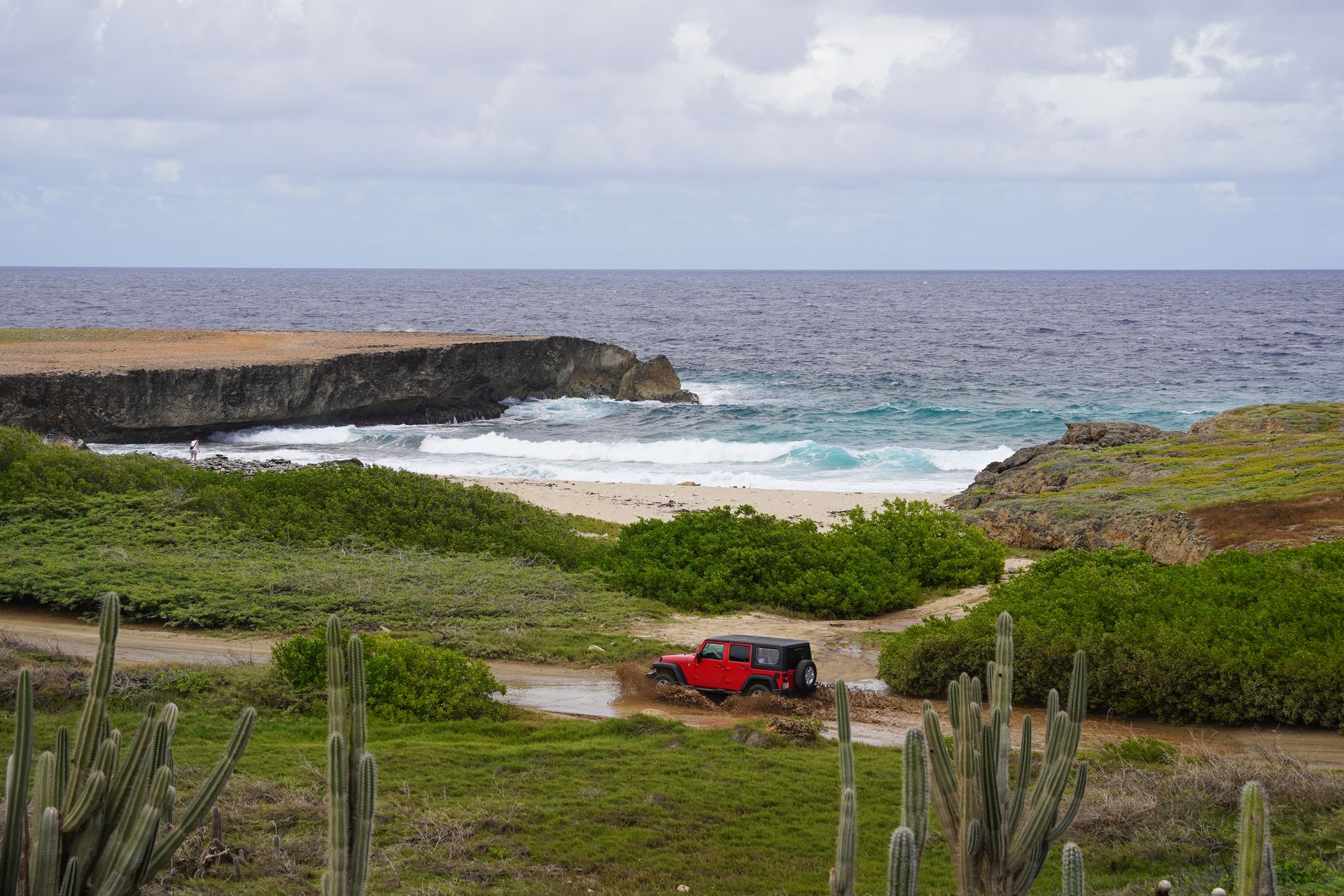 A jeep driving through muddy water on a dirt road next to the coast