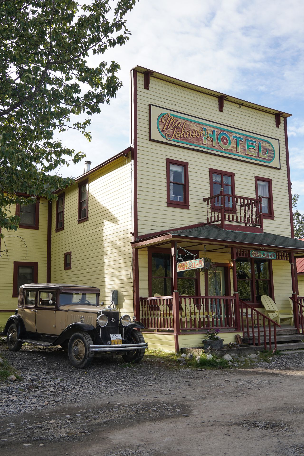 The exterior of Ma Johnson's Hotel, with a porch and a vintage car sitting next to the building