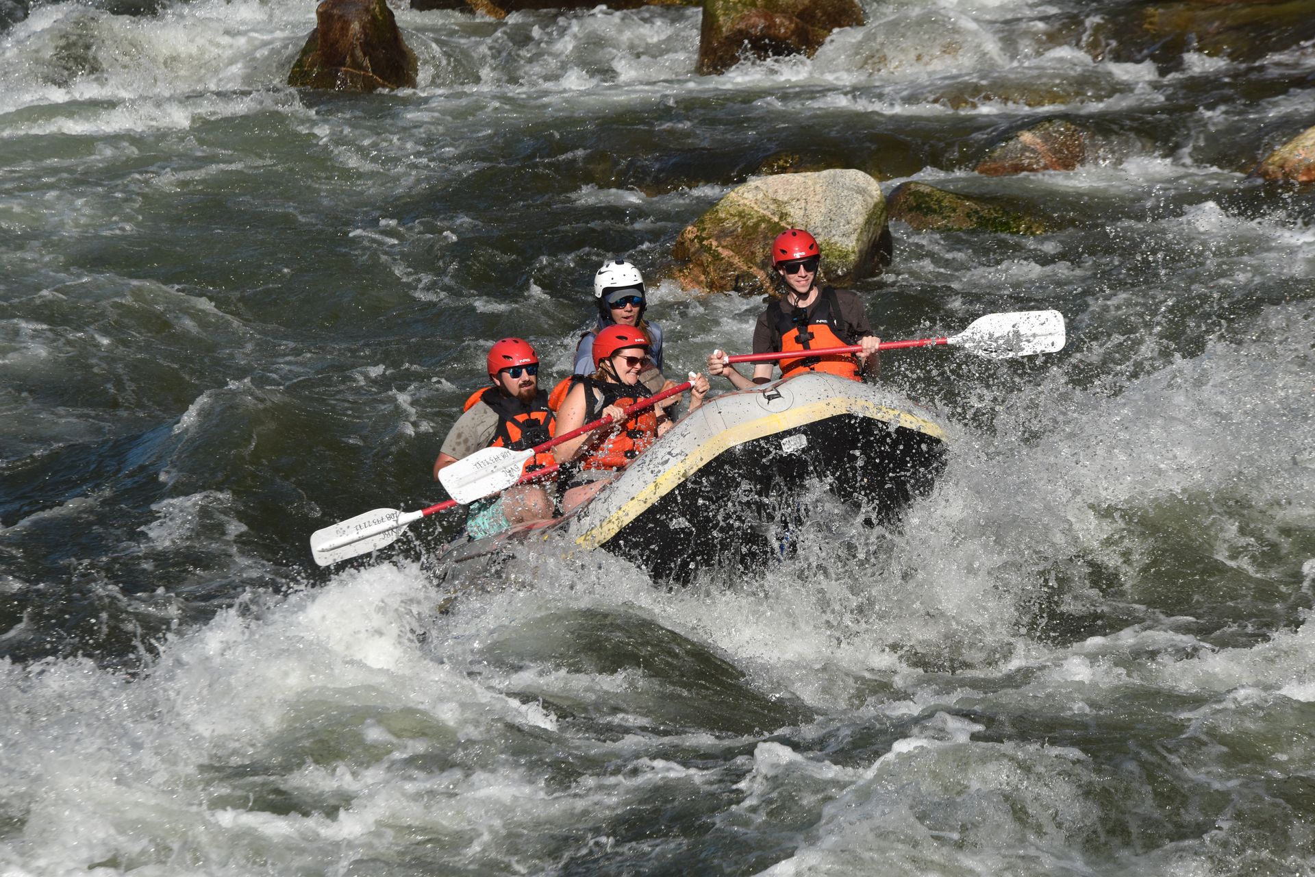 Lydia, two others and a rafting guide going over a rapid while white water rafting on the Payette River