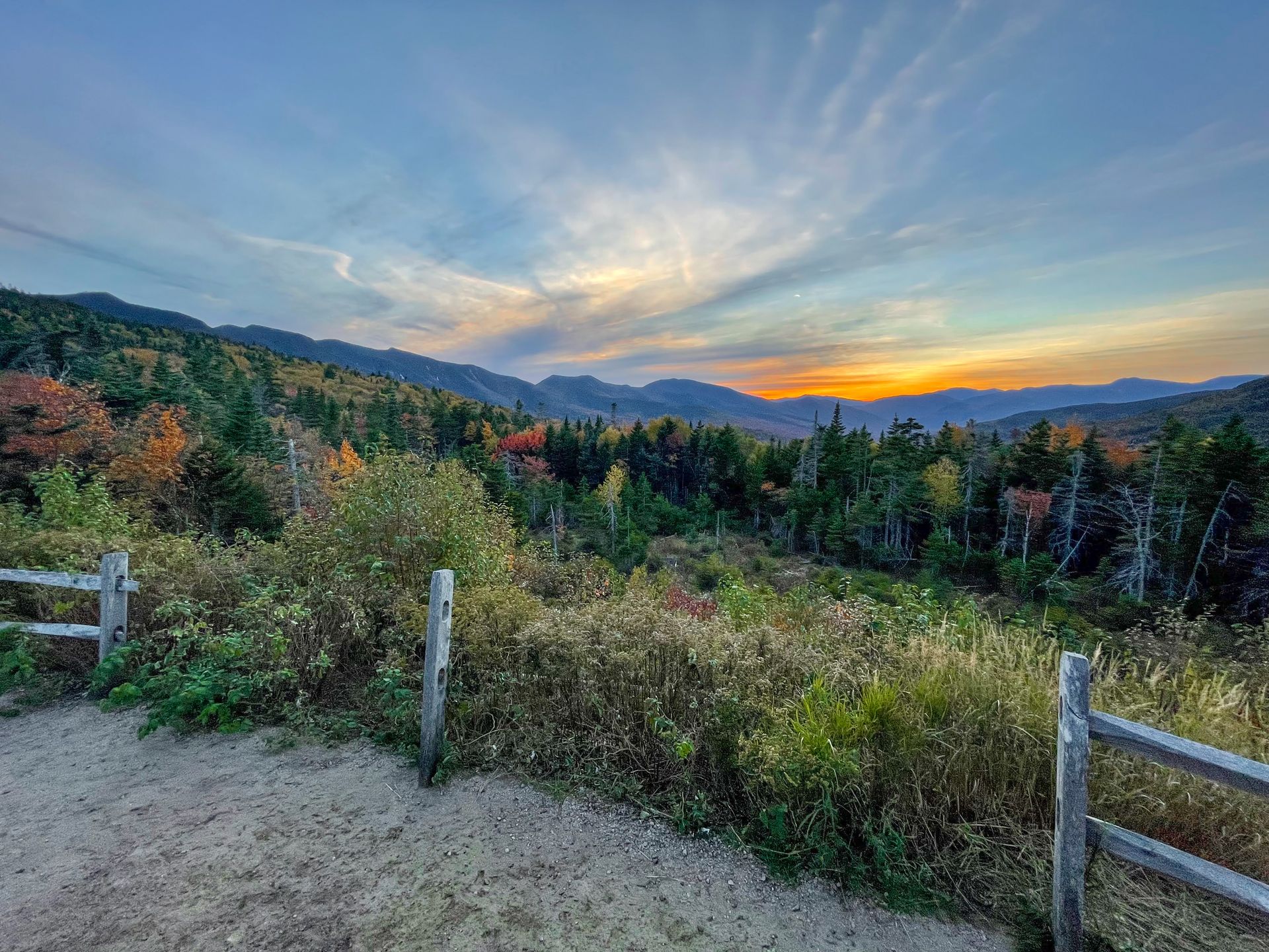 Mountains in the distance, fall colors and the sun setting in the sky at the Pemigewasset Overlook