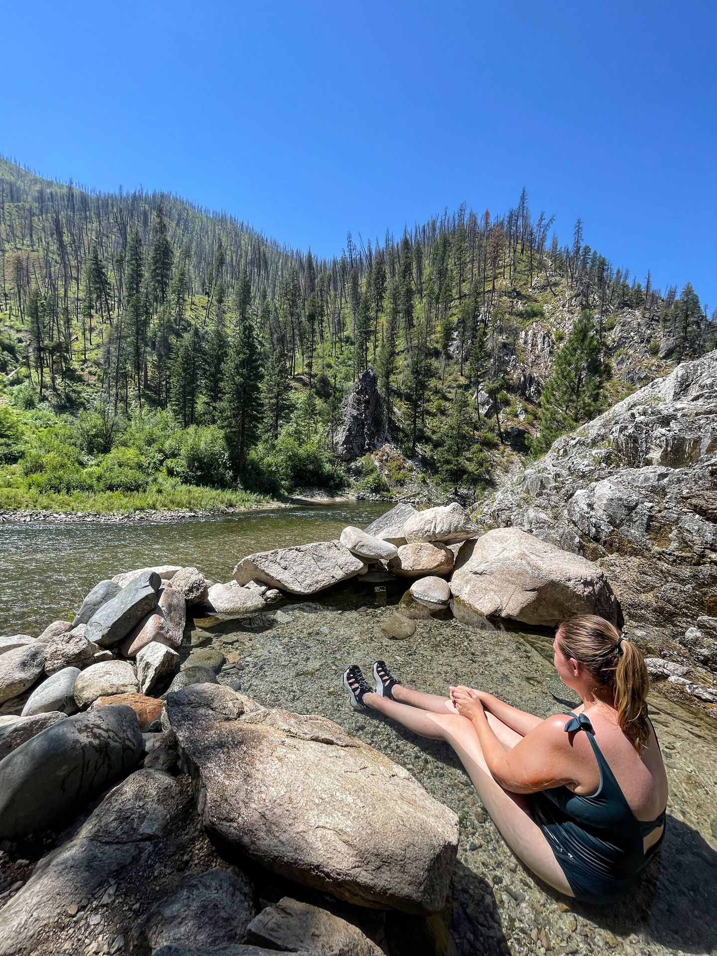 Lydia sitting in a small pool of water, facing out towards the Payette River
