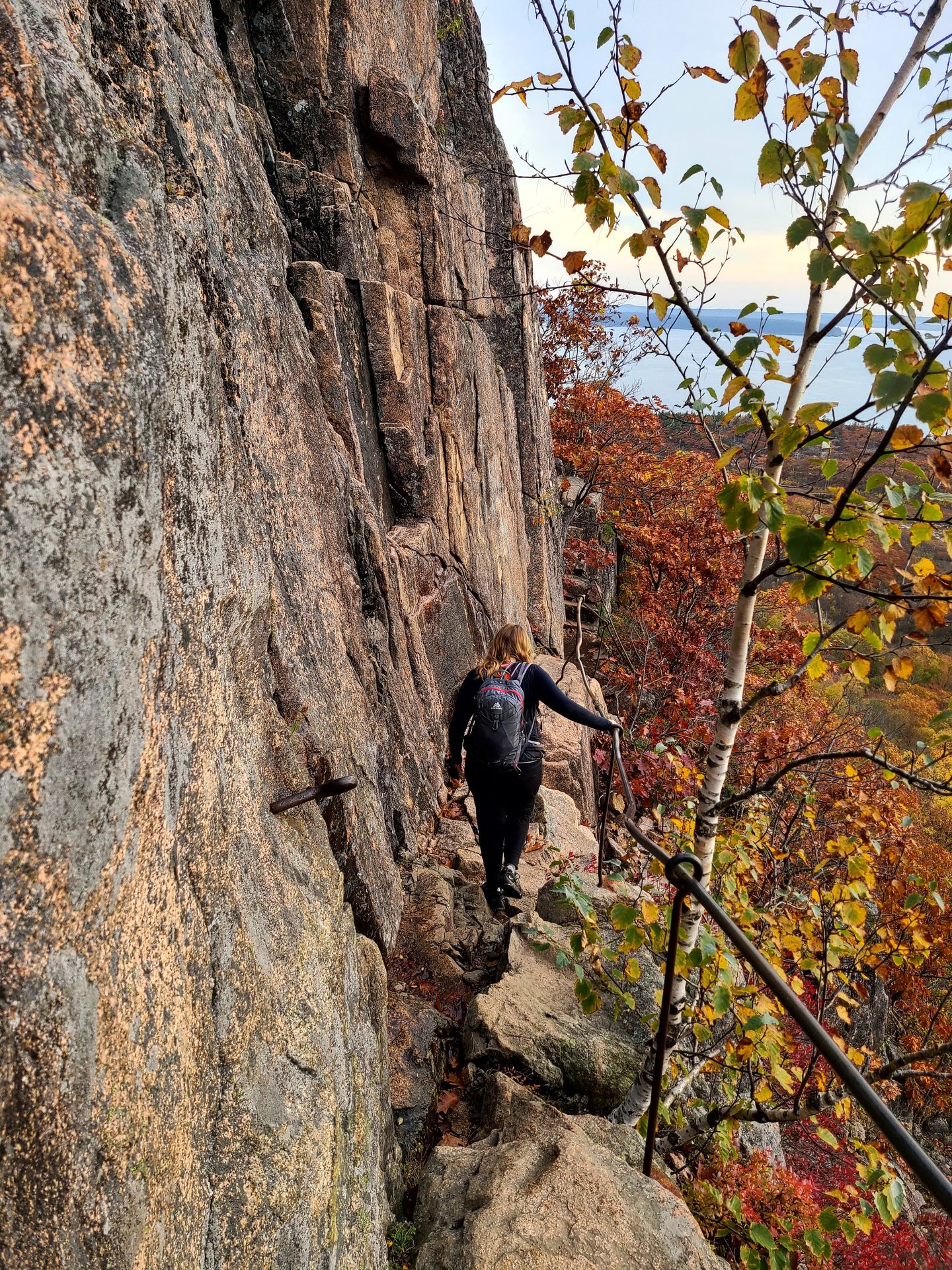 Lydia hiking on a narrow cliff path and touching a metal railing on the Precipice Trail
