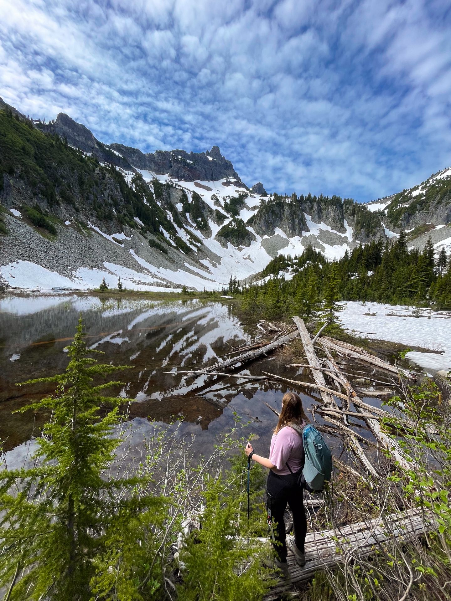 Lydia standing on a log and looking at lake with a reflection of a snowy mountain in it