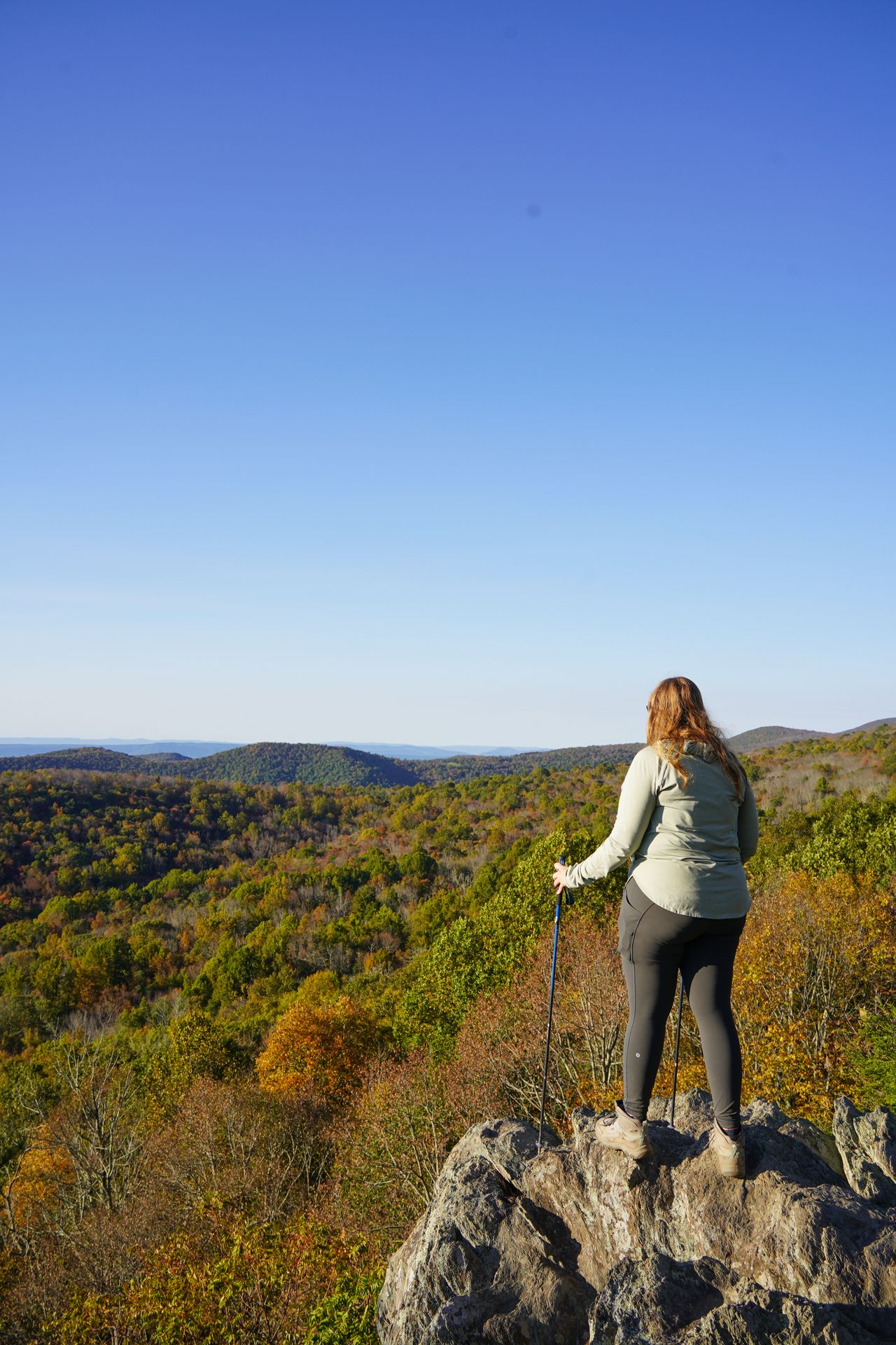 Lydia standing on a rock and looking out at rolling mountains that are a mix of green with orange foliage