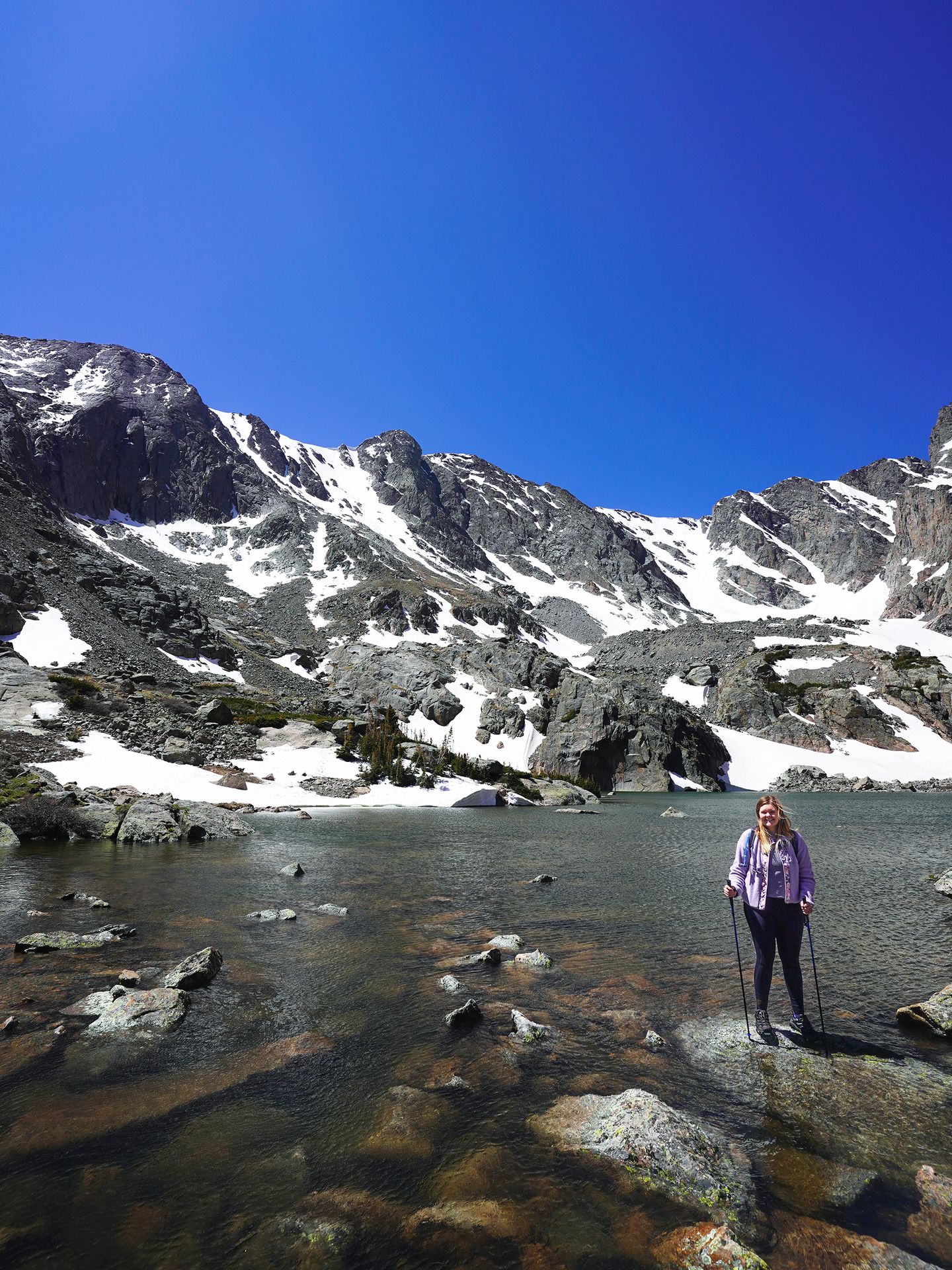 Lydia standing in front of Sky Pond. The mountain in the background is partially covered in snow