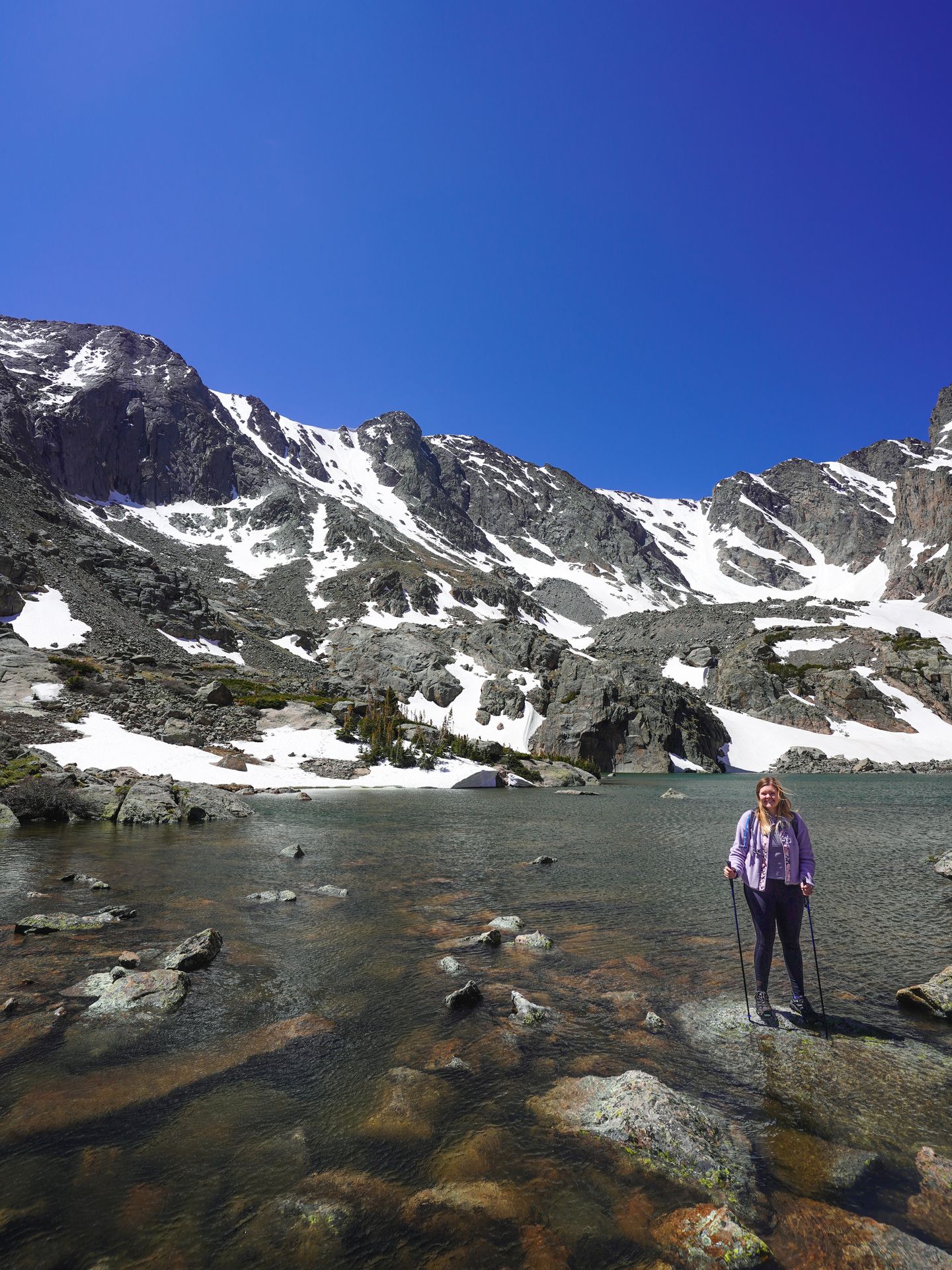 Lydia sitting next to Sky Pond. There are various drifts of snow along the mountainside.