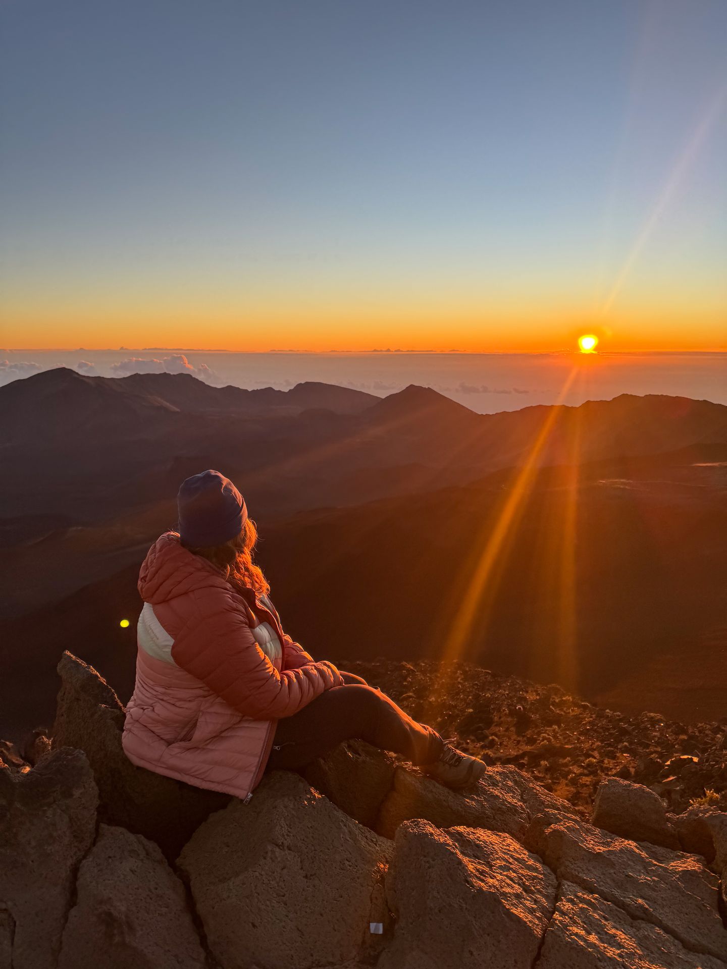 Lydia sitting on a rock and looking out at the sunrise over the Haleakala Crater