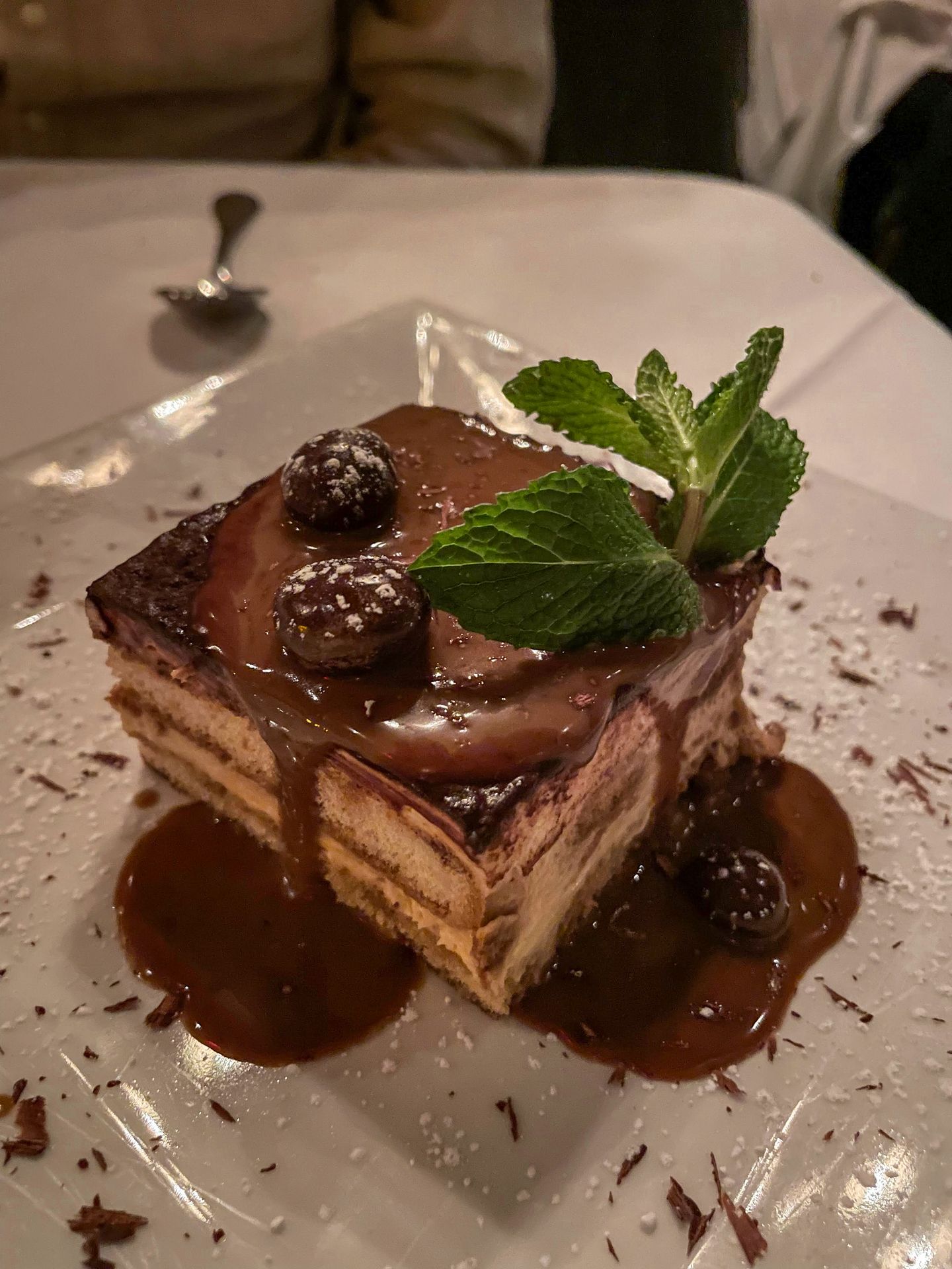 A tiramisu dessert from Mamma Maria. There is a green garnish on top and a chocolate sauce dripping from the top.