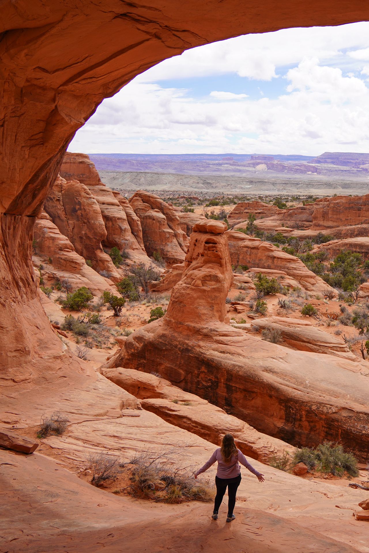 Lydia standing under an orange arch and looking out at rocky views on the Tower Arch Trail in Arches National Park