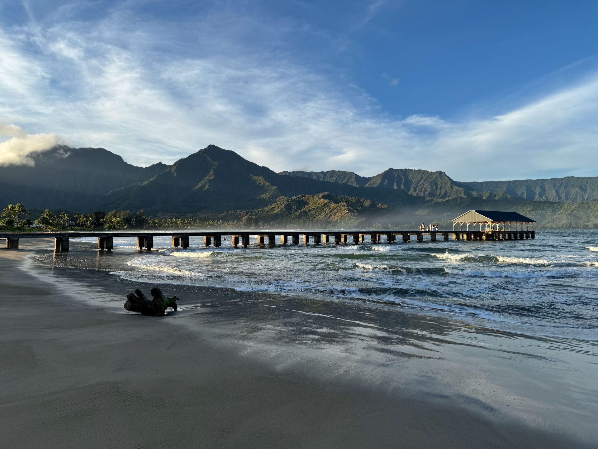 A long dock extending into the ocean, in front of a green coast with jagged cliffs