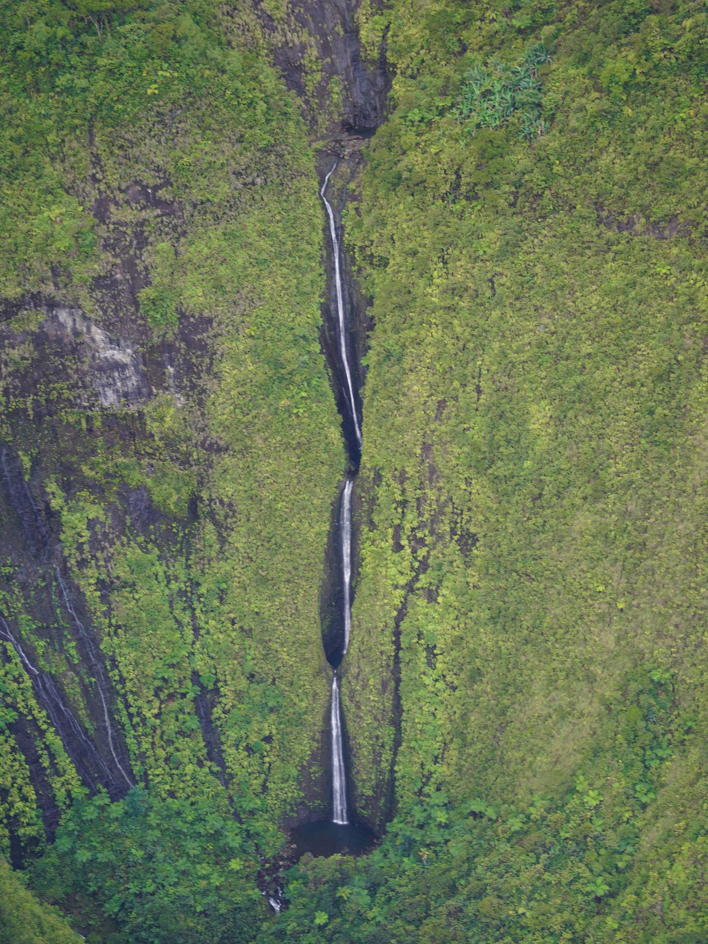 A tall waterfall that cascades down into multiple pools, seen from above on a helicopter tour