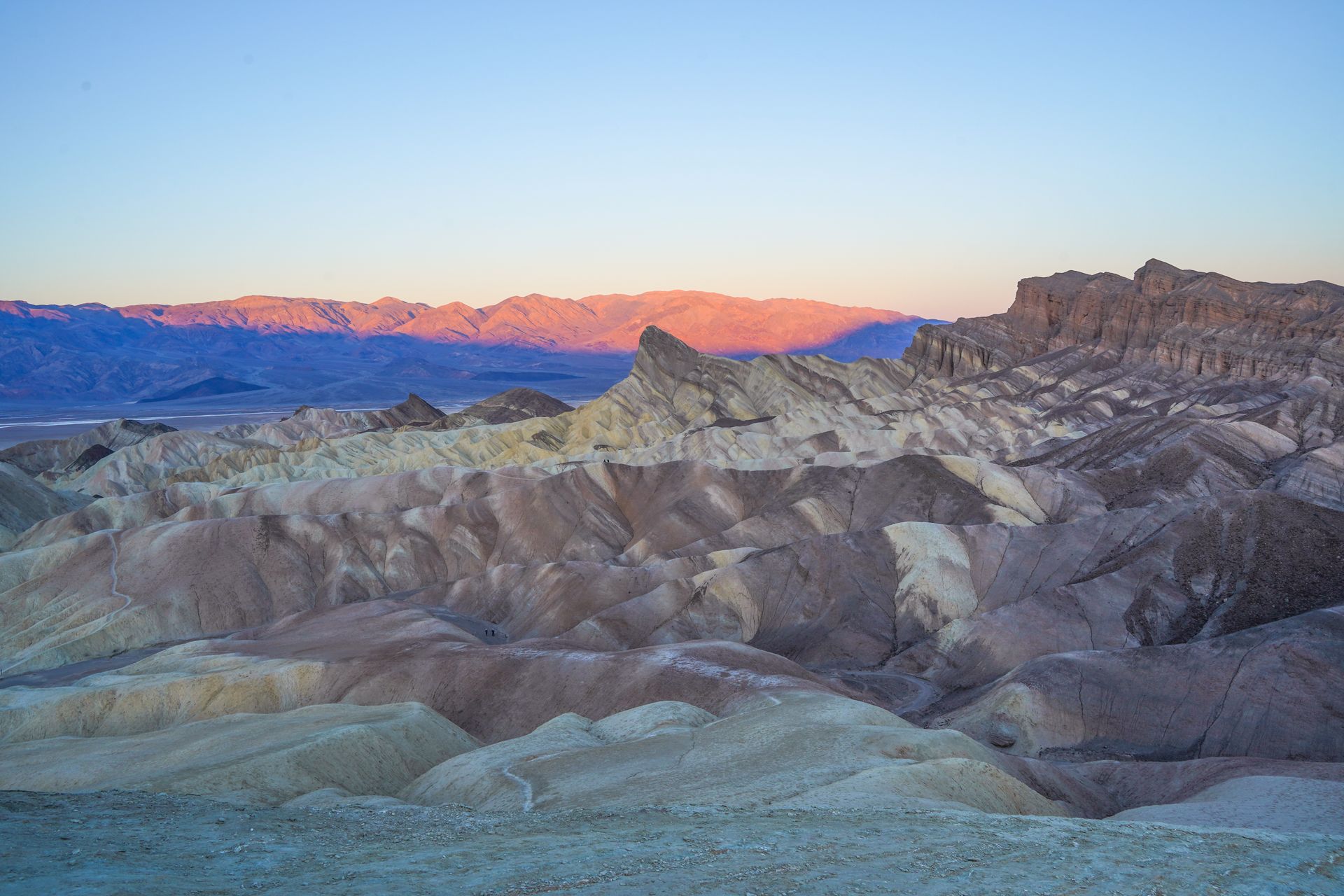 A mountain glows pink in the distance, and stripey rocks make up the view in the foreground, at Zabriskie Point in Death Valley